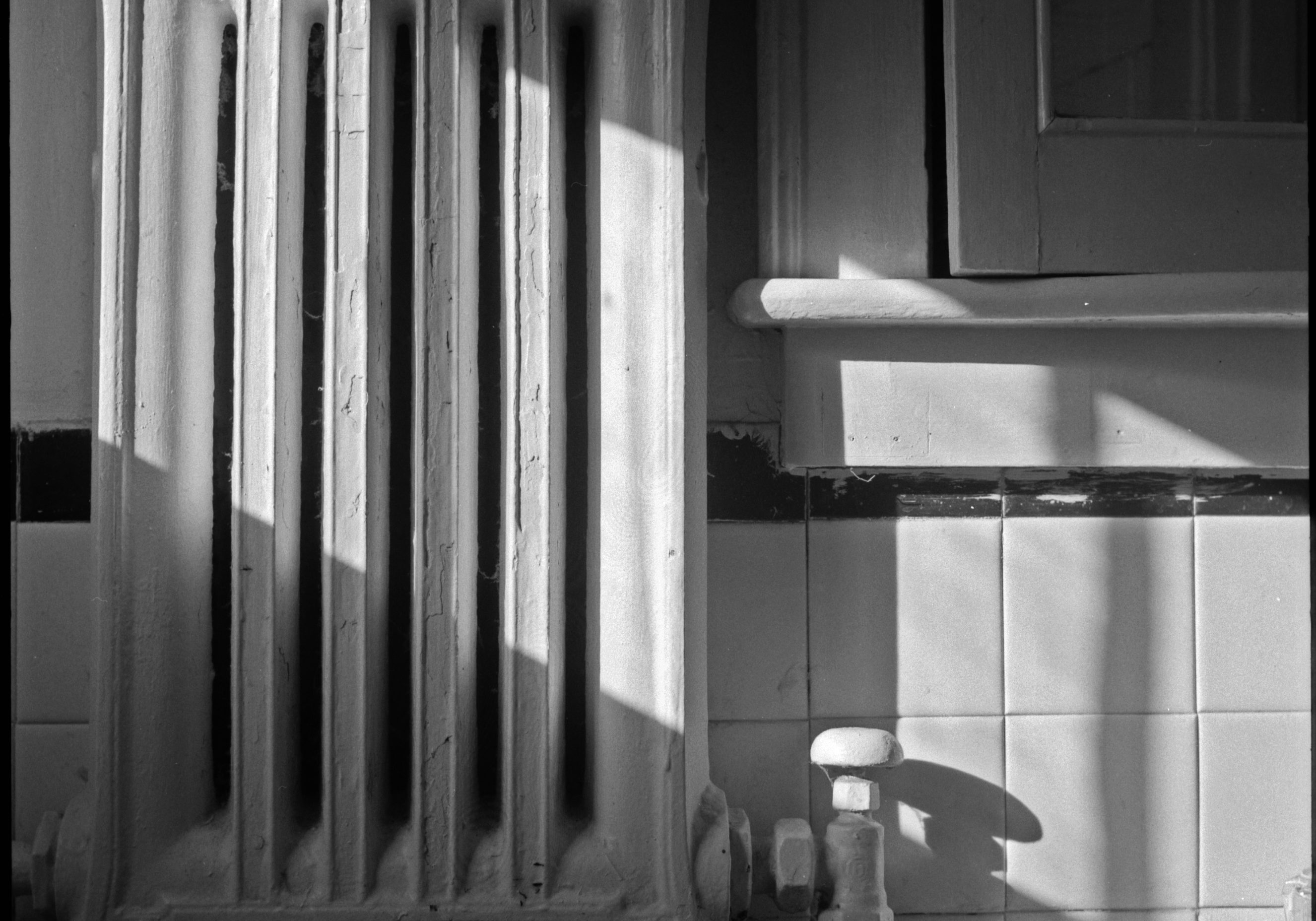 image of a bathroom radiator hanging on white tiles with a slant of sun falling across it and onto the sink.