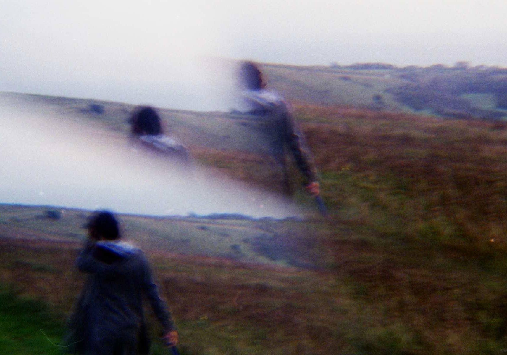 image of a woman with her back turned from the camera walking on a hill or cliff full of dry brown grass. the image has her overlaid a few times because of a film mistake.