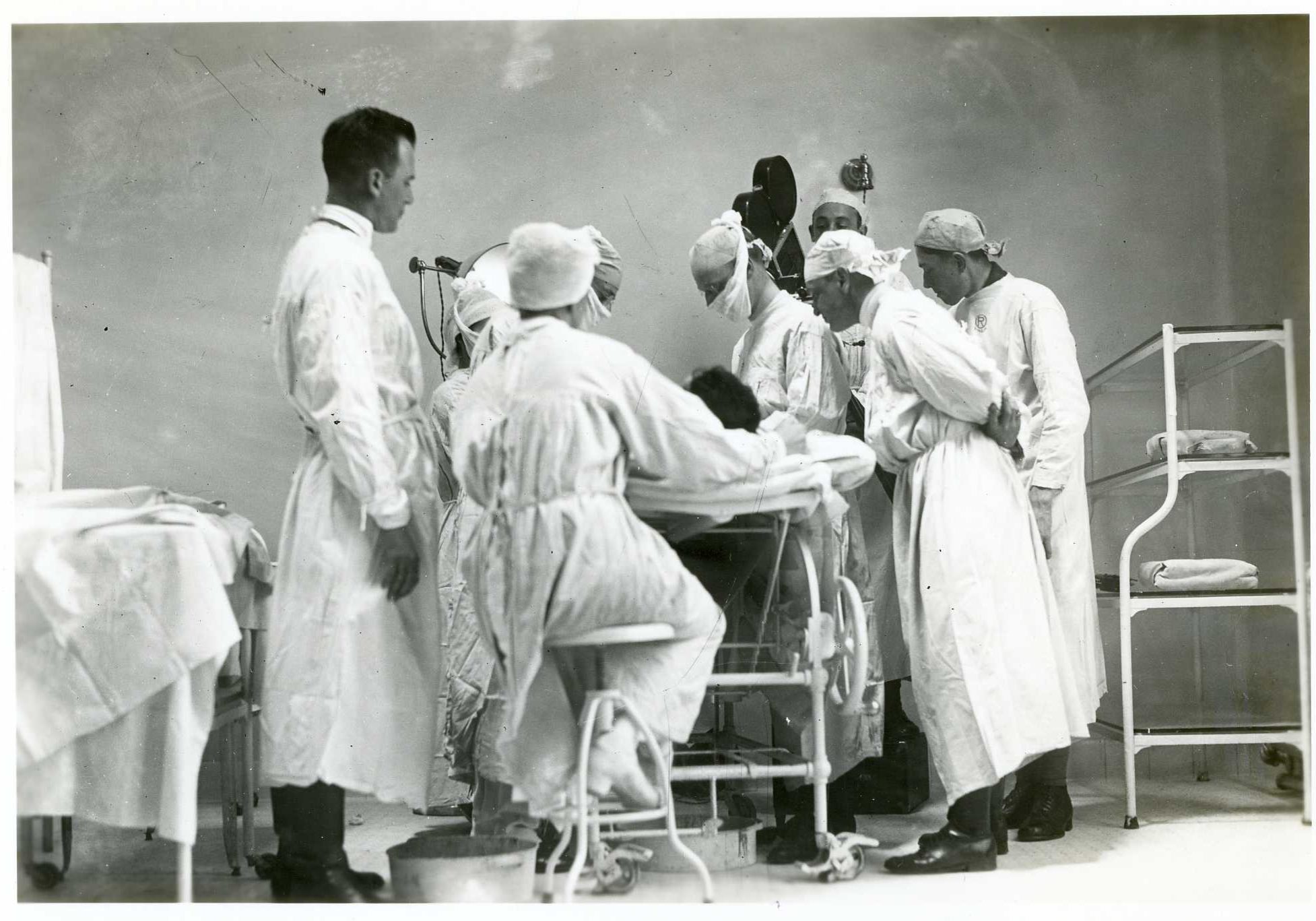 old image of doctors and nurses gathered around operating table.