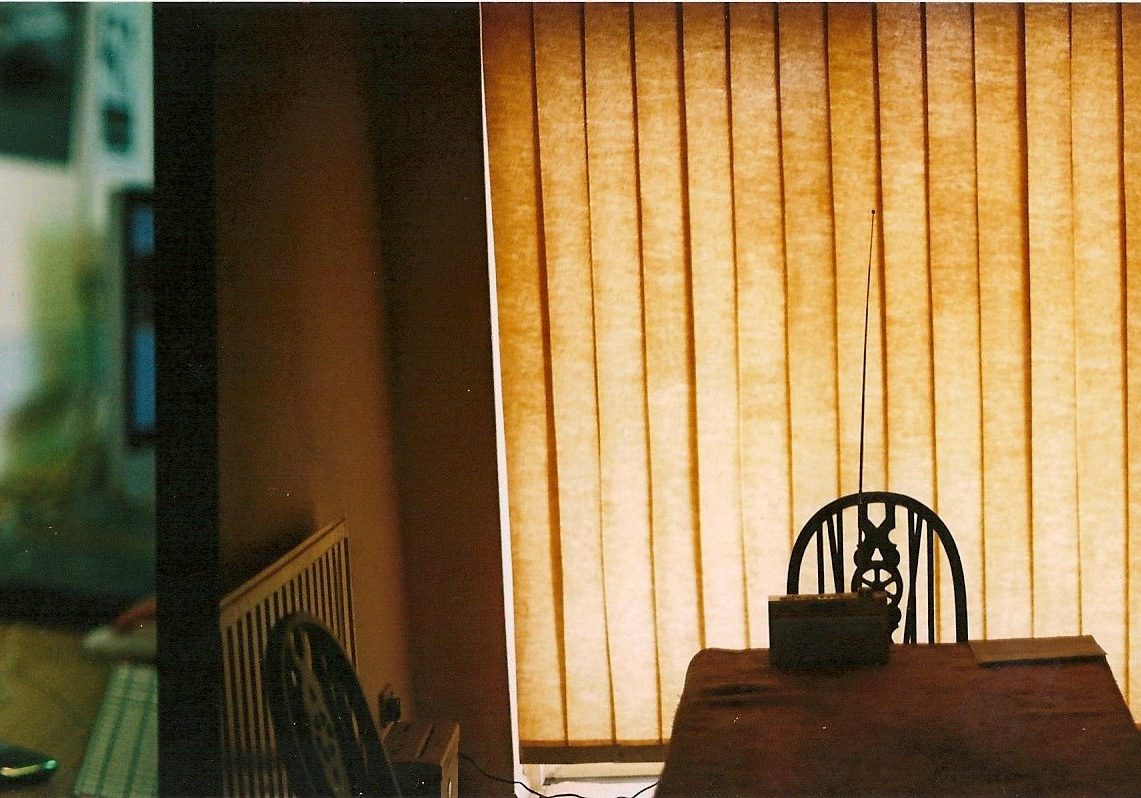 Interior of a house, a table and chair illuminated against a yellow blind behind it.
